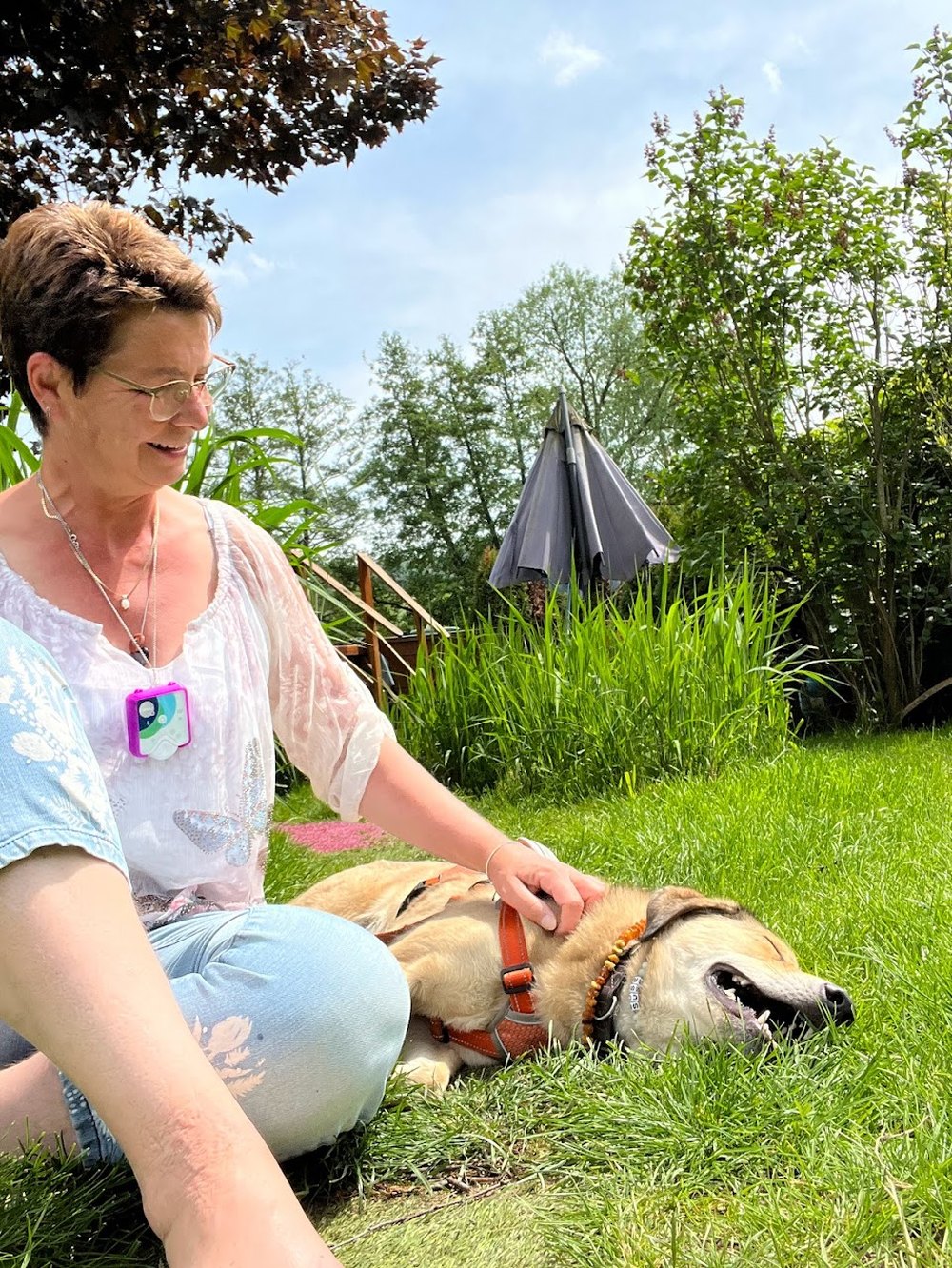 Kerstin Hartwigsen im Garten mit ihrem Hund, der entspannt im Gras liegt